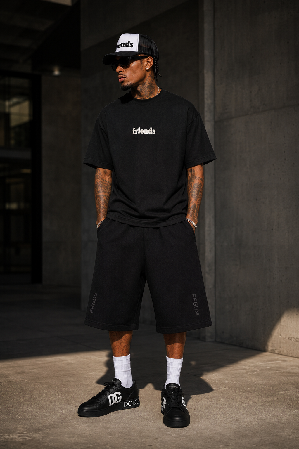 Model wearing black Friends of the Program T-shirt and FRNDS PRGRM shorts in a concrete editorial setting