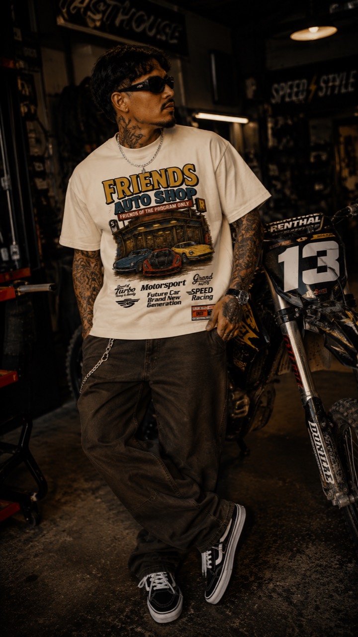 Model wearing the cream Friends Auto Shop tee beside a dirt bike in a garage