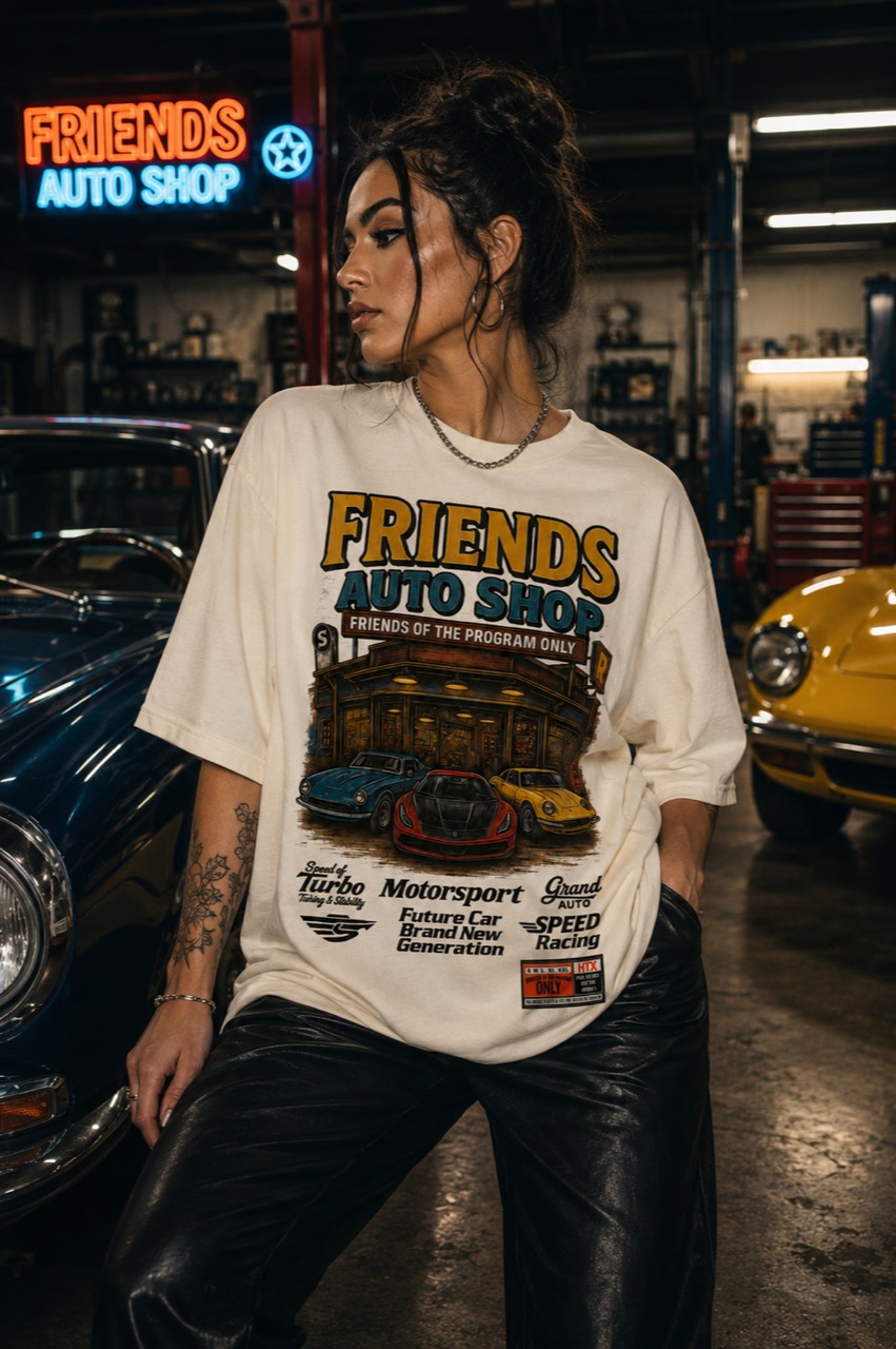 Model wearing the cream Friends Auto Shop tee inside a garage with classic cars