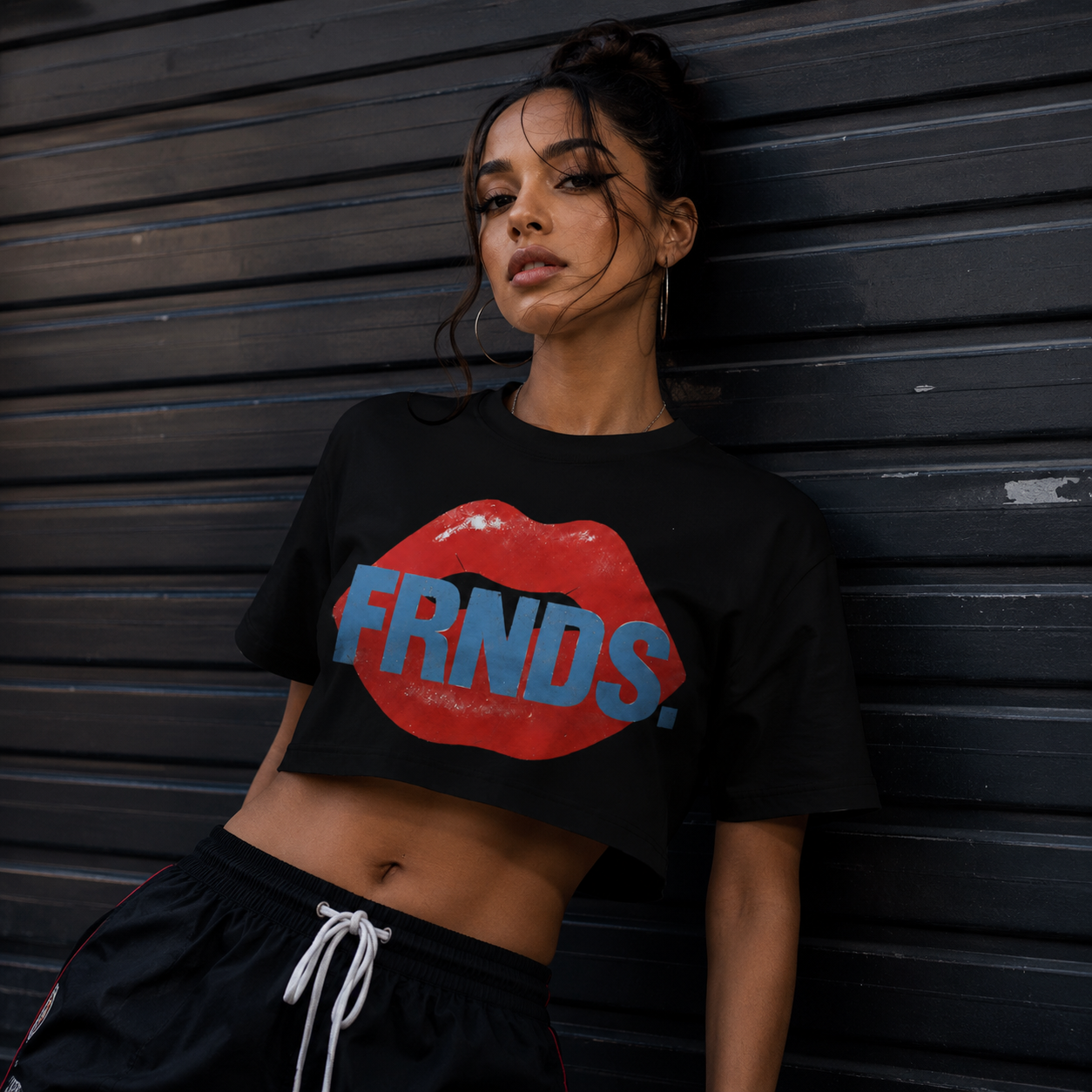 Model wearing the black FRNDS lips crop top against a dark roll-up door